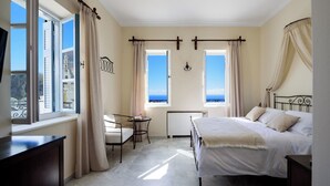 A bedroom with a bed, a desk, and two windows with curtains. - Ikio Concept Santorini (Santorini)