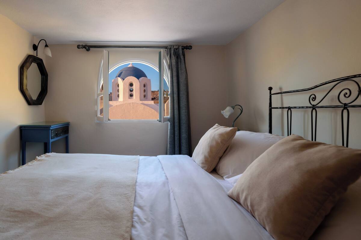 A bedroom with a bed, a window with curtains, a nightstand, and a wall-mounted light fixture.