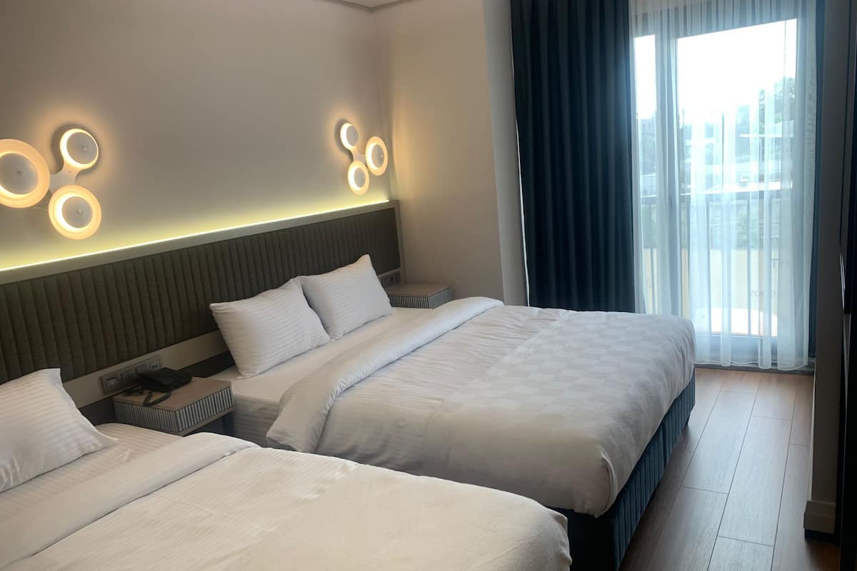 A hotel room with two beds, a modern headboard, and a large window with curtains.
