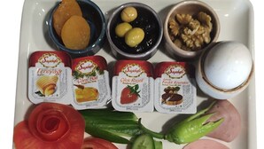 A tray with various food items including sliced tomatoes, cucumbers, French fries, a slice of ham, cheese, and several small containers of condiments. - Theodosius Hotel (Istanbul)