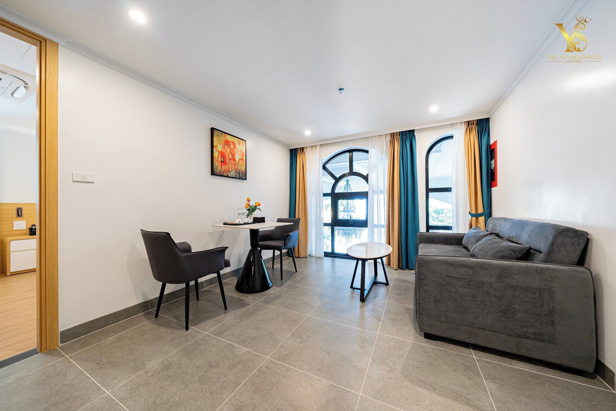 Una sala moderna con un sofá gris, una mesa de comedor con sillas y un ventanal con cortinas.