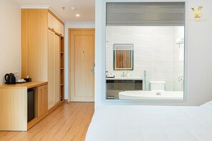 A hotel room with a wooden wardrobe, a small kitchenette, a large window with a view of a bathroom, and a bed. - The Yen Residences Danang (Da Nang)