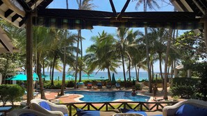 Ein Poolbereich mit Liegestühlen und Sonnenschirmen, umgeben von Palmen und Blick aufs Meer.