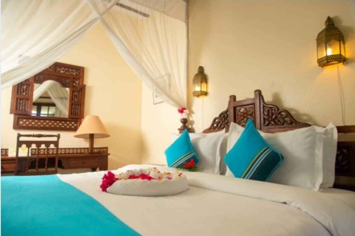 Habitación de hotel con una cama, una mesita de noche, una lámpara, un espejo y una lámpara de pared.