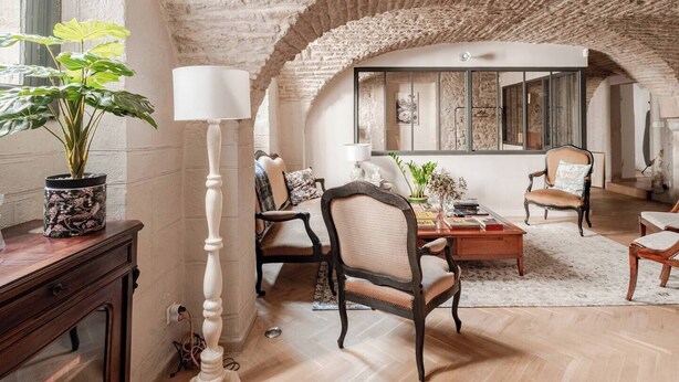 A spacious room with a high arched ceiling, a wooden floor, and a large mirror reflecting the room. There are several chairs and a table with books and a lamp. - In the heart of town exceptional apartment nestled in an hôtel particulier. (Dijon)