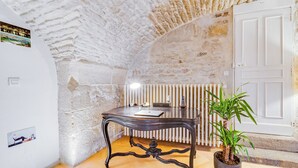 A room with a stone wall, a wooden table, a radiator, and a door. - In the heart of town exceptional apartment nestled in an hôtel particulier. (Dijon)