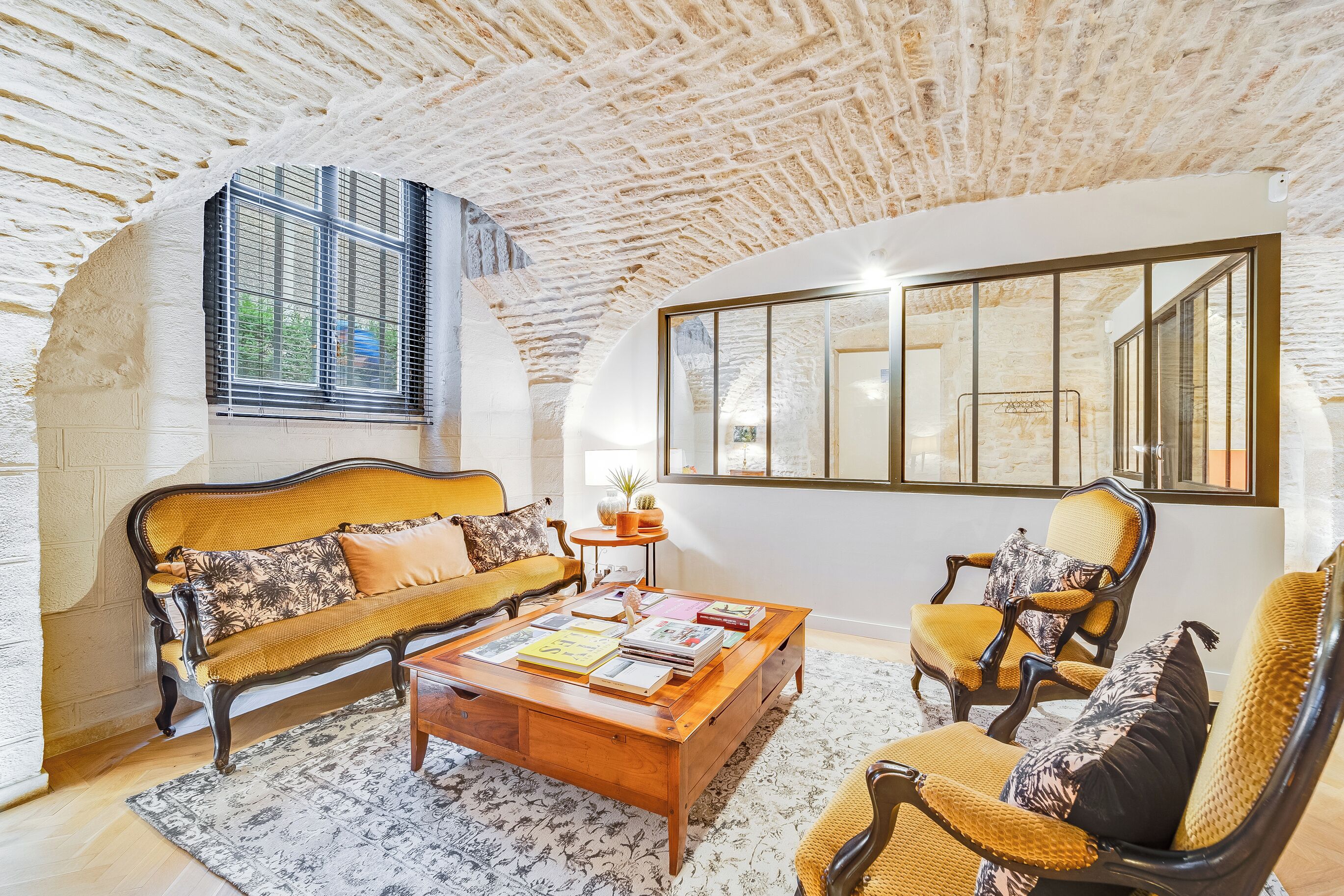 A cozy living room with a stone ceiling, a sofa, a coffee table with books, and a large window.