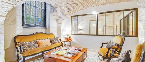 A cozy living room with a stone ceiling, a sofa, a coffee table with books, and a large window.