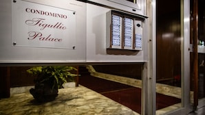 Letrero de 'CONDOMINIO Tigullio Palace' con un panel de control y una planta en maceta.