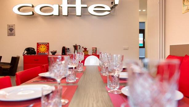 Un comedor con una mesa larga preparada para una comida, un sofá rojo y un letrero en la pared que dice "caffe".