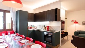Cocina compacta con armarios oscuros, horno empotrado y comedor con sillas rojas y una mesa para cuatro.