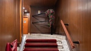 Interior de madera con una escalera de mármol, escalones alfombrados en rojo y un arreglo floral colgante.