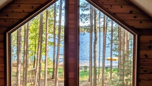 Una cabaña con dos ventanas amplias que dan vistas a un bosque y un lago.