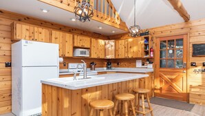 A wooden cabin-style kitchen with a central island, bar stools, a refrigerator, a microwave, and a sink.