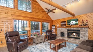 A log cabin interior with a fireplace, leather chairs, a television, and a bookshelf.