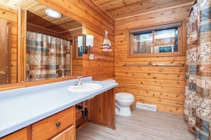 Baño de cabaña de madera con lavabo, espejo, inodoro y ventana.