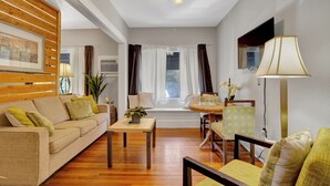A living room with a sofa, coffee table, and chairs, a window with curtains, a ceiling fan, and a lamp.