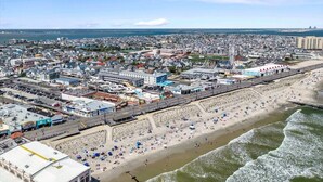 Une vue aérienne d’une ville côtière, avec une vaste plage, une promenade et une zone urbaine dense, caractérisée par des bâtiments et des infrastructures.