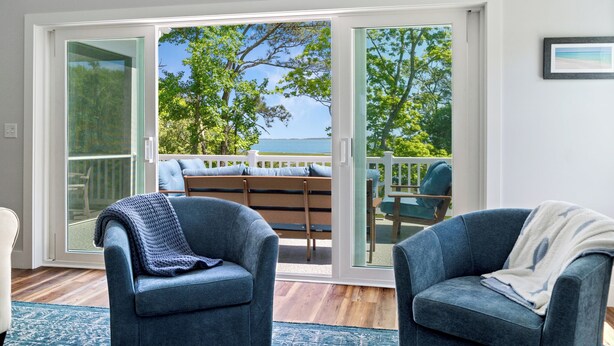 A room with a large sliding glass door leading to an outdoor deck with a view of the sea. There are two blue armchairs and a bench with cushions. - Assateague Holiday House Nature & Luxury Combined (Berlin)