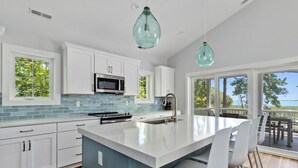 A modern kitchen with white cabinets, a blue backsplash, and a large island with bar stools. - Assateague Holiday House Nature & Luxury Combined (Berlin)