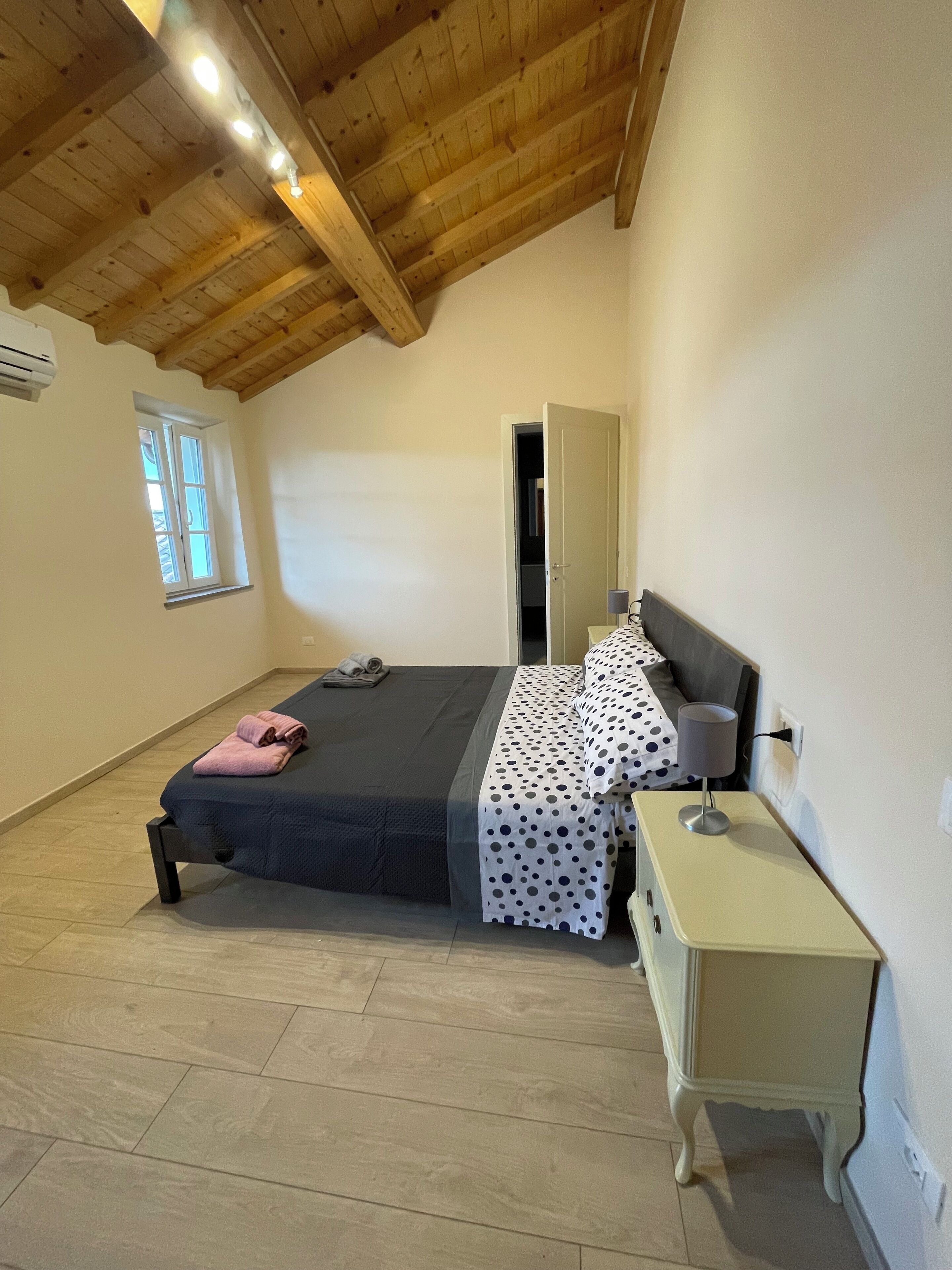 Een slaapkamer met een bed, nachtkastje, lamp, spiegel en raam.
