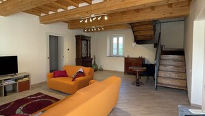 A spacious living area with a wooden ceiling, a sofa set, a television, and a staircase leading to an upper level.