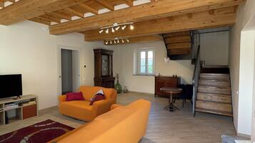 Un'ampia zona giorno con soffitto in legno, un divano, una televisione e una scala che conduce a un piano superiore.