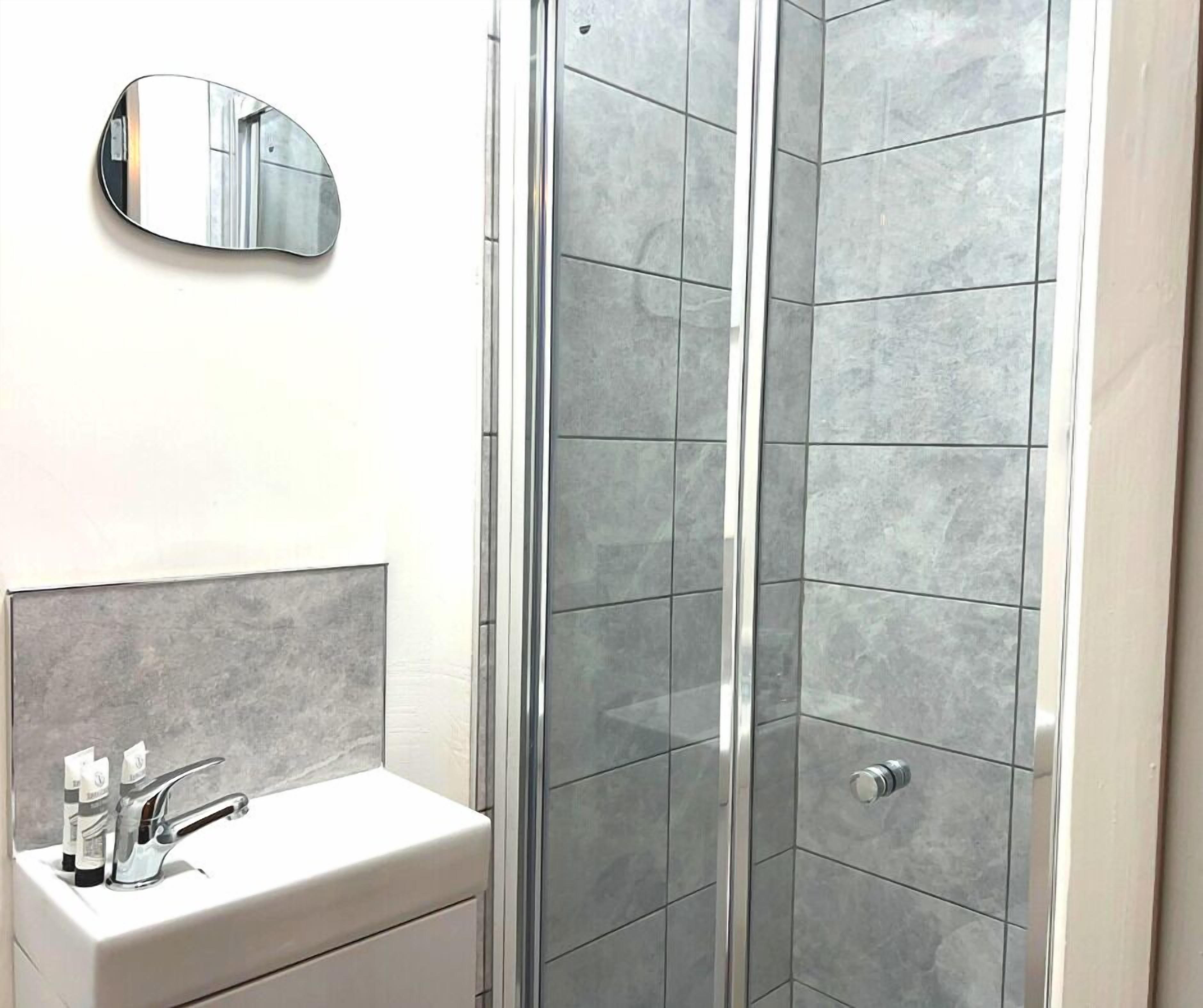 A bathroom with a white sink, a mirror, and a shower with grey tiles.