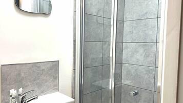 A bathroom with a white sink, a mirror, and a shower with grey tiles.