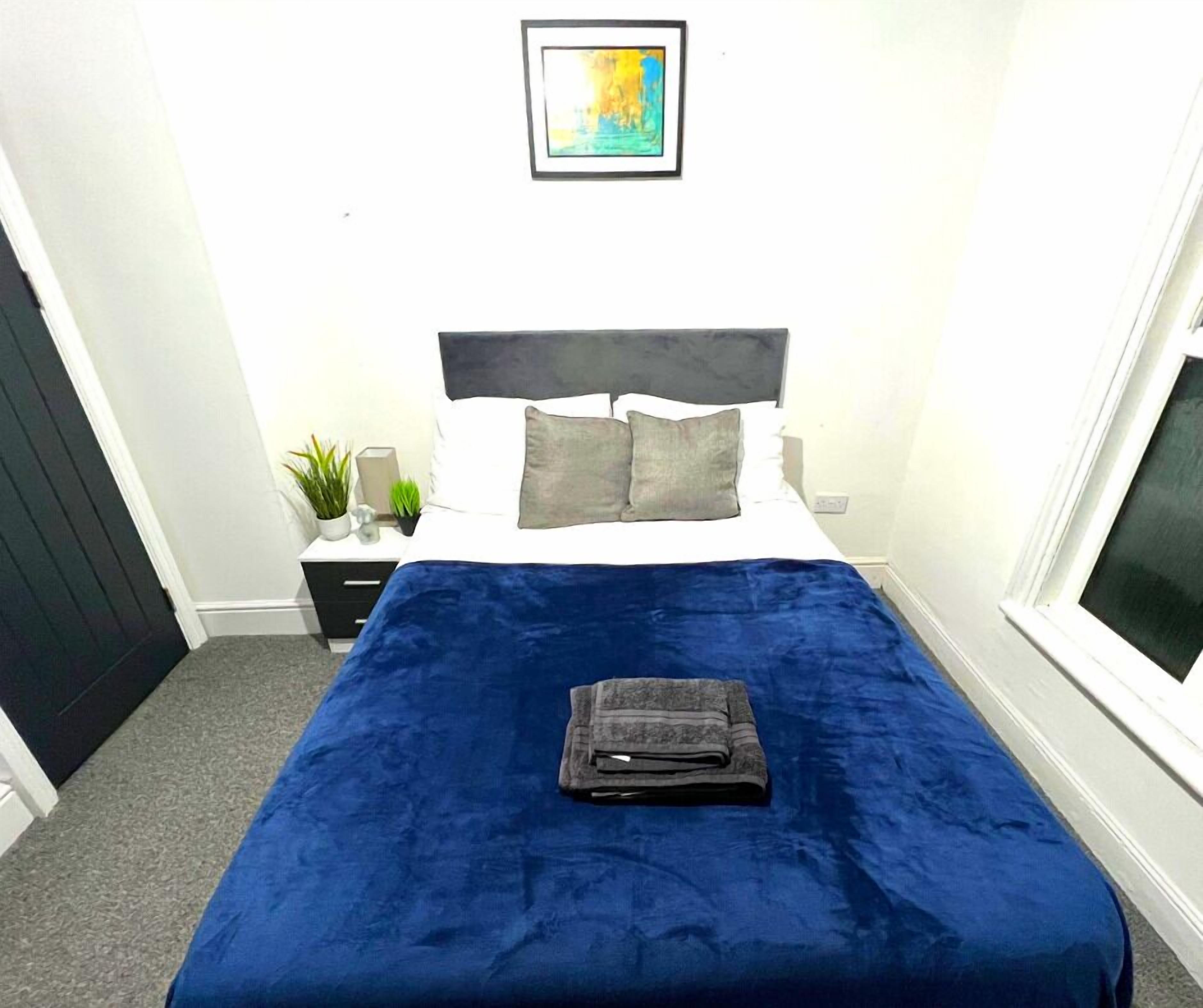 Una camera da letto con una coperta blu, una testiera grigia e un quadro appeso al muro.