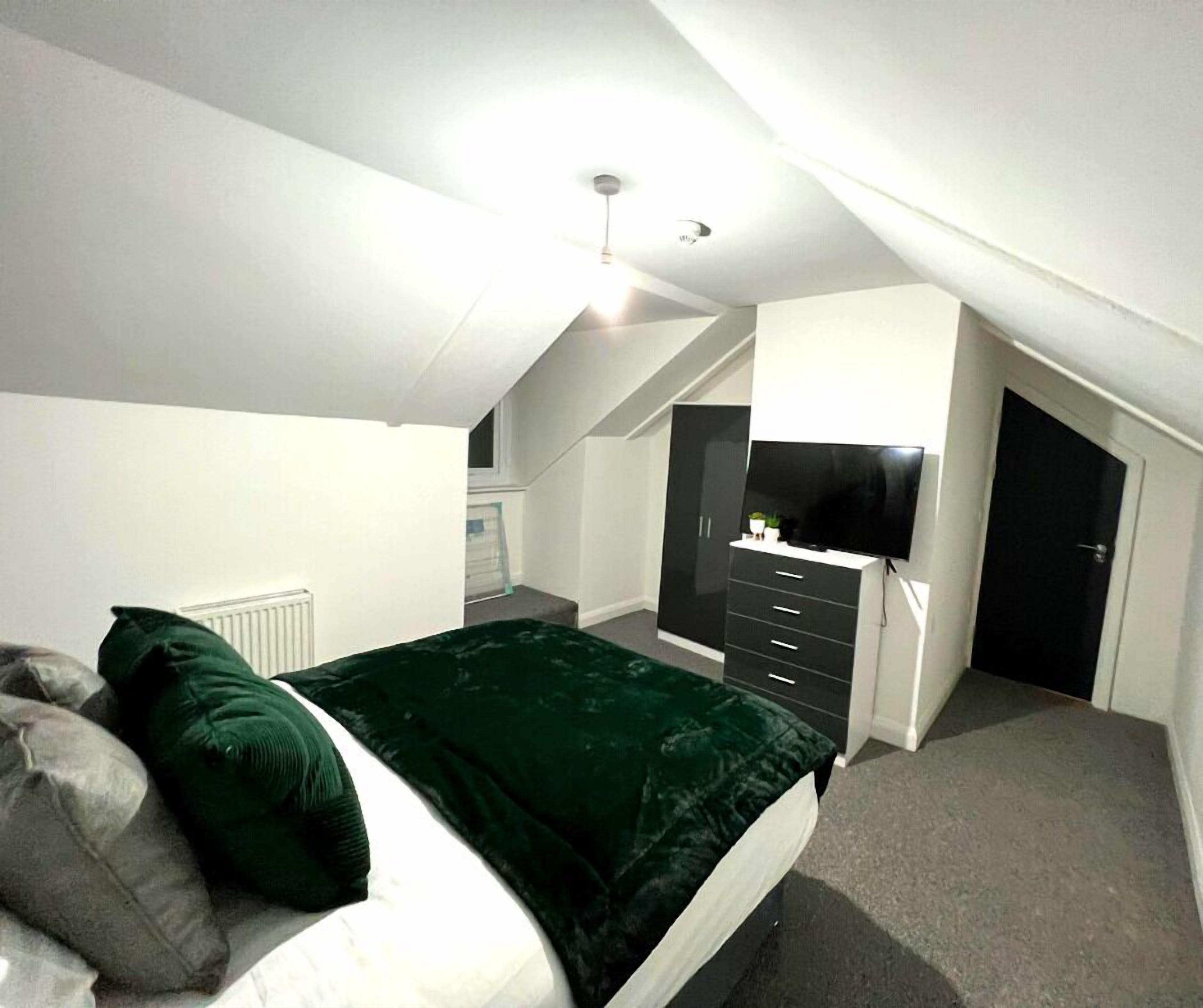A bedroom with a bed, a dresser, a television, and a staircase.