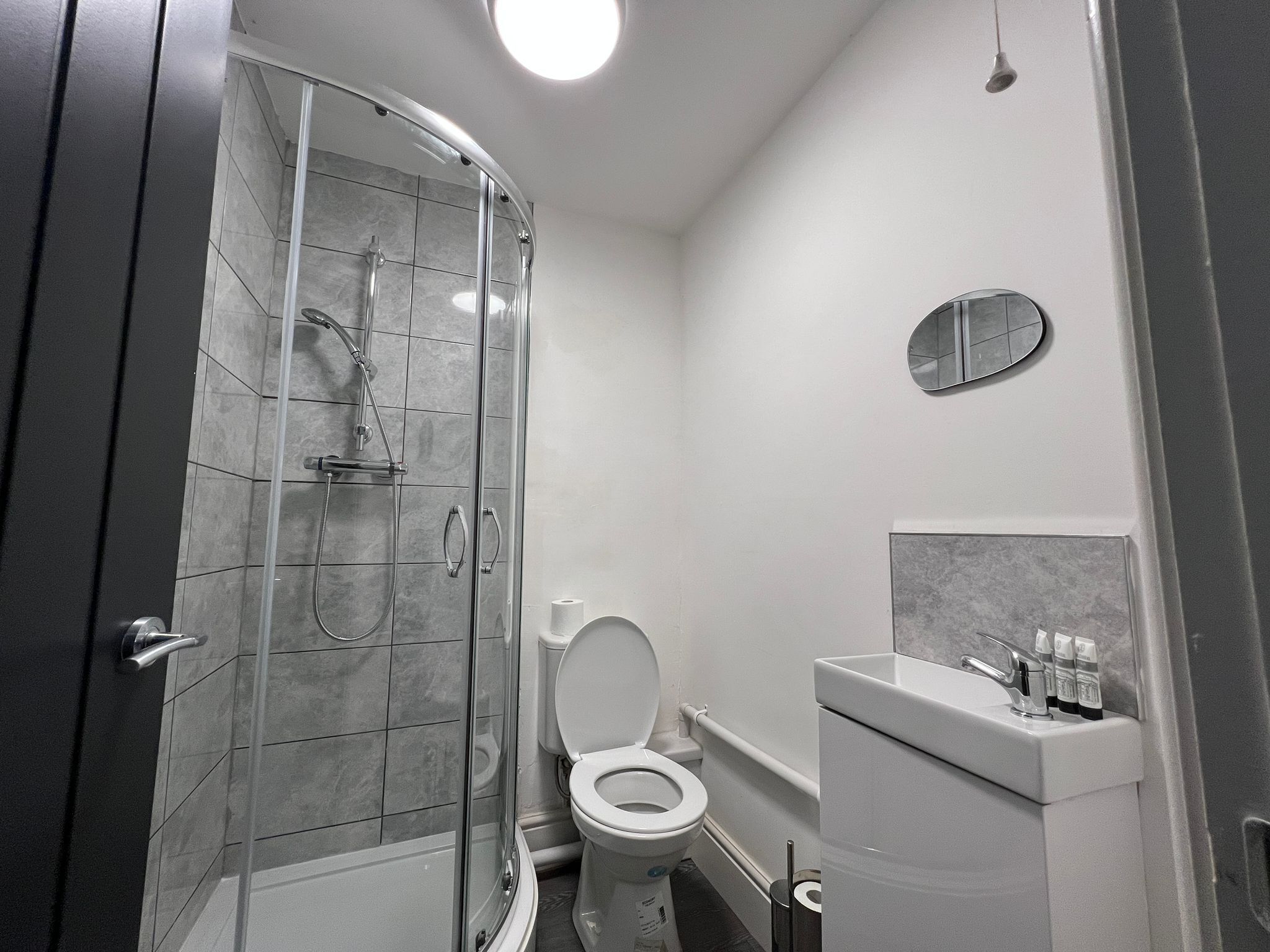 Et moderne badeværelse med en glasafskærmet brusekabine, toilet og håndvask med toiletartikler.