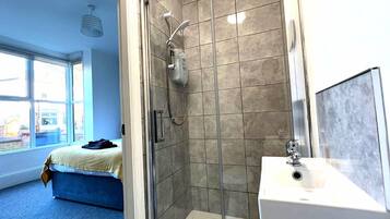 Un baño moderno con cabina de ducha de vidrio, un lavabo blanco y una cama con cabecero azul.