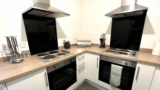 A modern kitchen with two black stoves, a built-in oven, and white cabinets. - Chantry Suites by SA Stays (Grimsby)