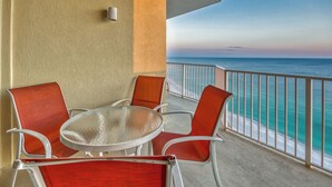 Un balcón con una mesa y sillas de vidrio, con vista a una playa y una vista despejada del océano.