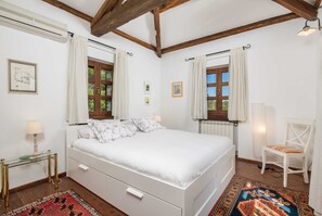 Un dormitorio con cama, una silla, una mesa y una ventana con cortinas.