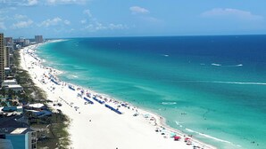 A beach with a long stretch of white sand, clear turquoise water, and a few buildings along the coastline.