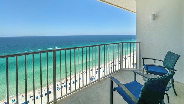A balcony with a view of a beach and ocean. There are two chairs and a table on the balcony.