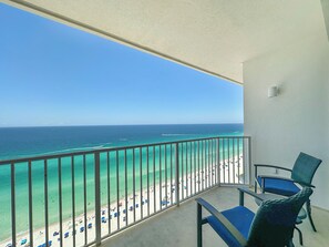 Un balcon avec vue sur une plage et l’océan. On y trouve deux chaises et une table.