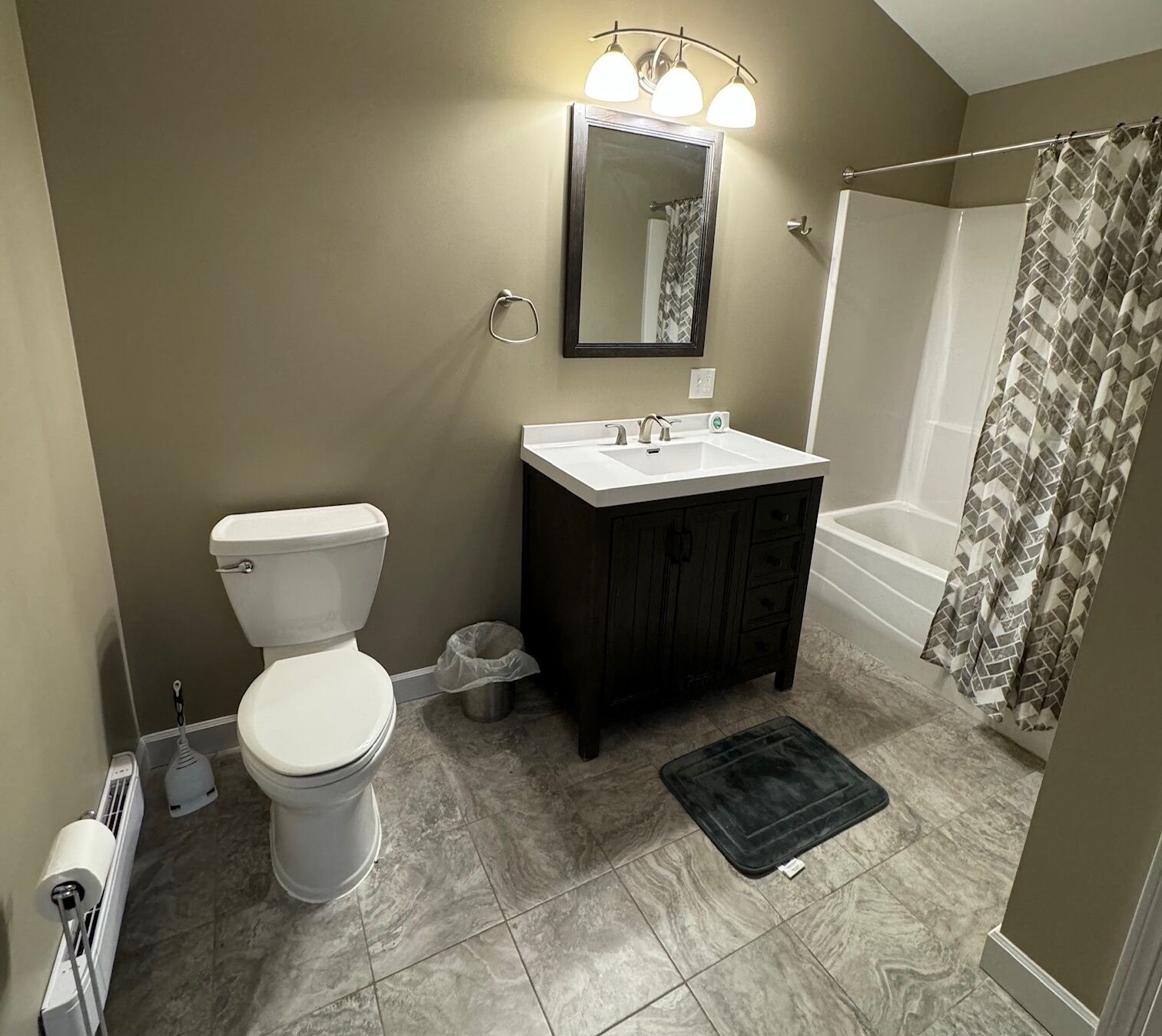 A bathroom with a toilet, sink, dark wooden cabinet, and a shower with a patterned curtain.