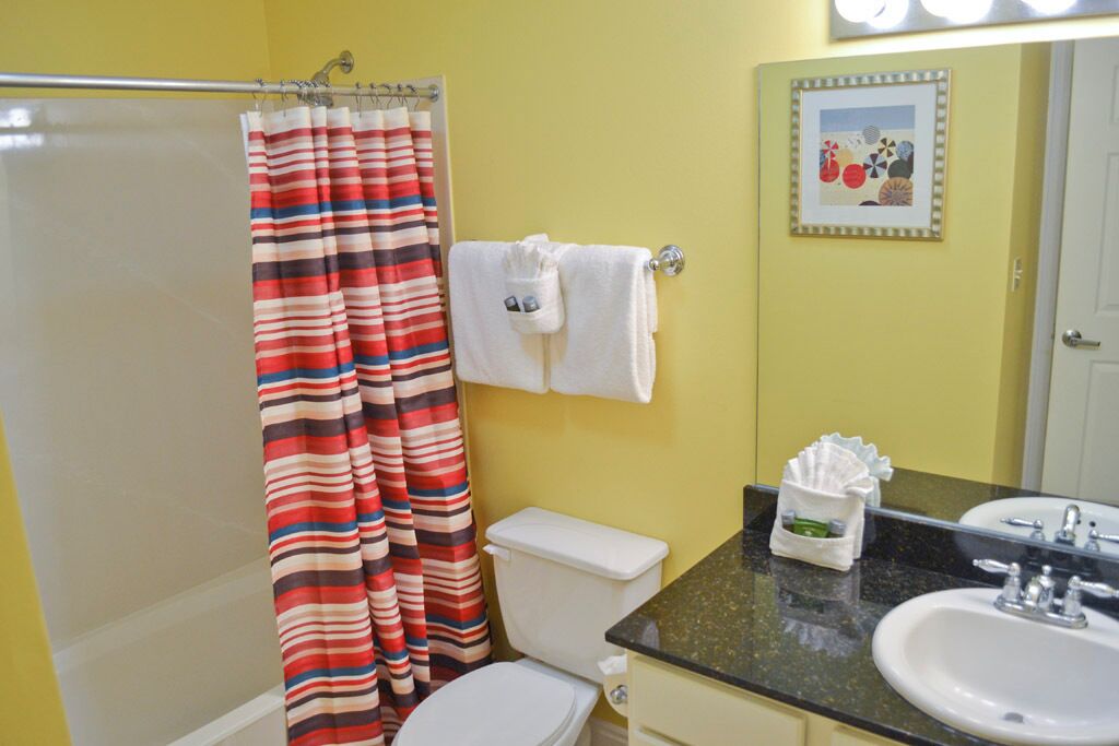 A bathroom with a striped shower curtain, a toilet, a sink, and a mirror.