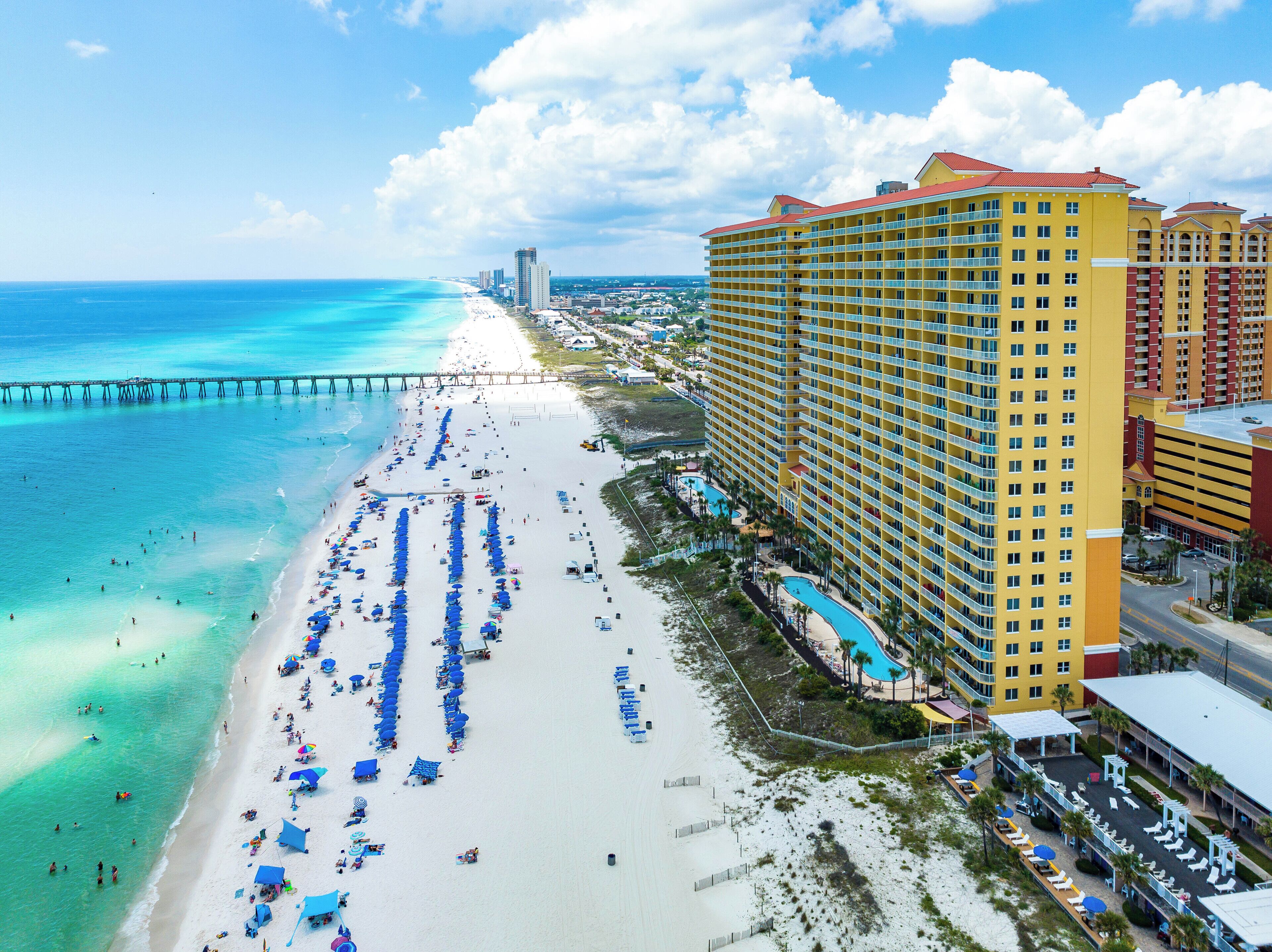 A beachfront hotel with multiple balconies, a pool area, and a pier extending into the ocean.