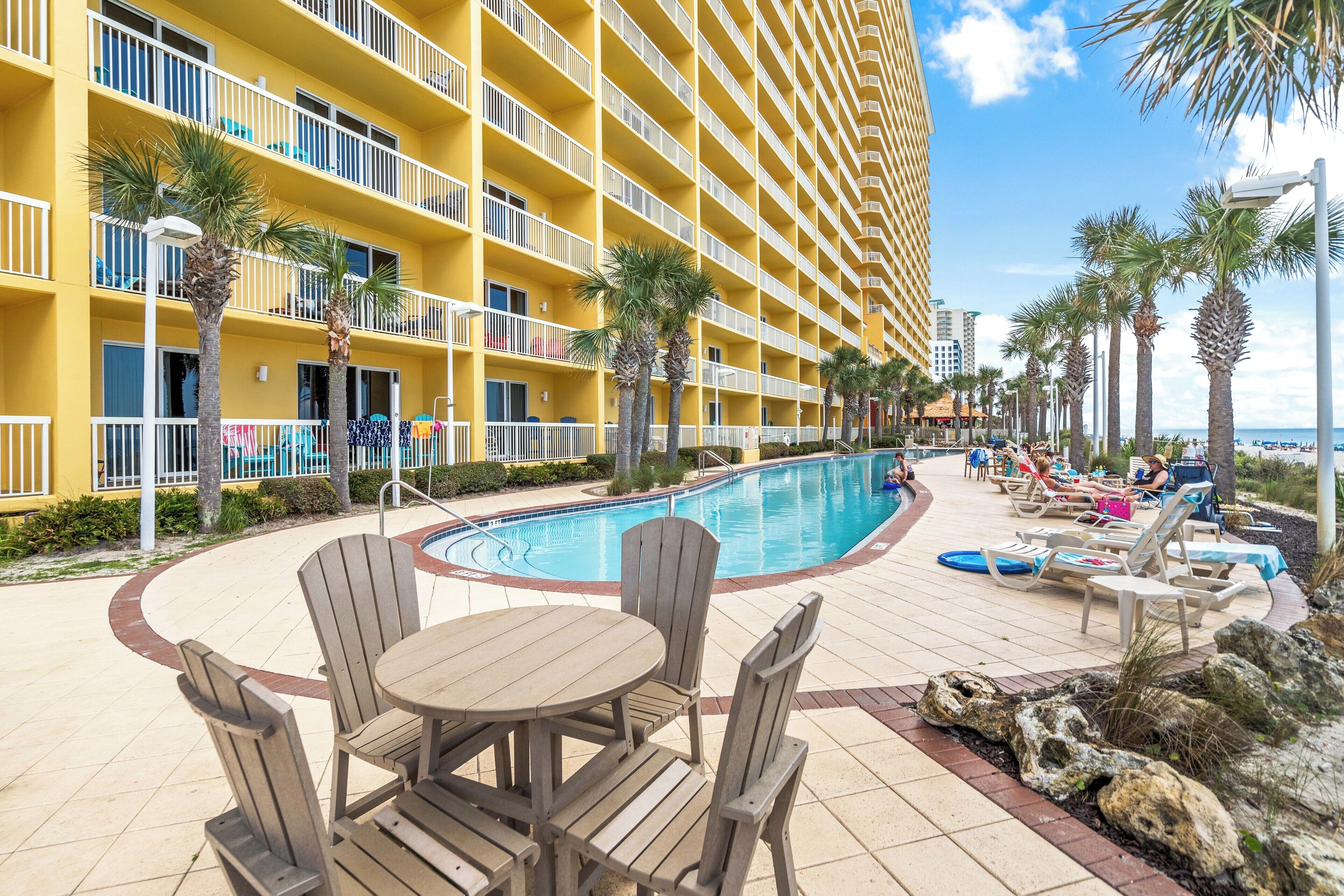 Un hôtel doté de nombreux balcons, d’un espace piscine avec des chaises longues et de palmiers.