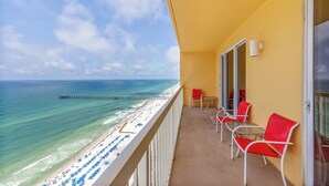 Een balkon met rode stoelen en een tafel, met uitzicht op een strand met parasols en een steiger.
