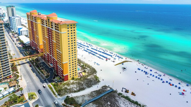 Een hoog hotel met uitzicht op het strand, een zandstrand met parasols en een heldere blauwe zee.