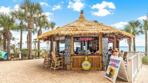 Een strandtentje met rieten dak, een bordje met 'COLD BEER' erop en een reclame voor ananassap.