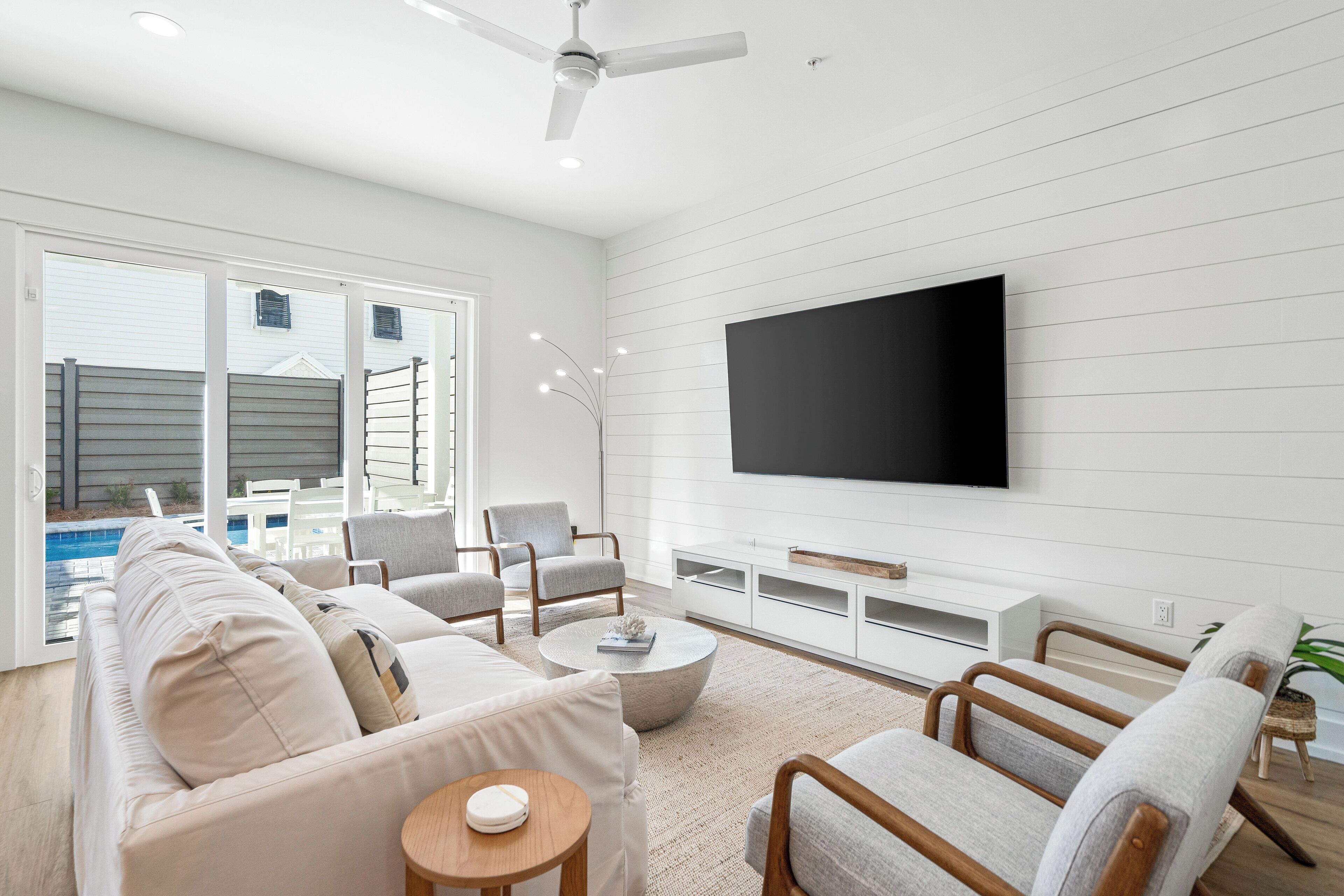 A modern living room with a flat-screen TV, a sofa, armchairs, a coffee table, and a ceiling fan.