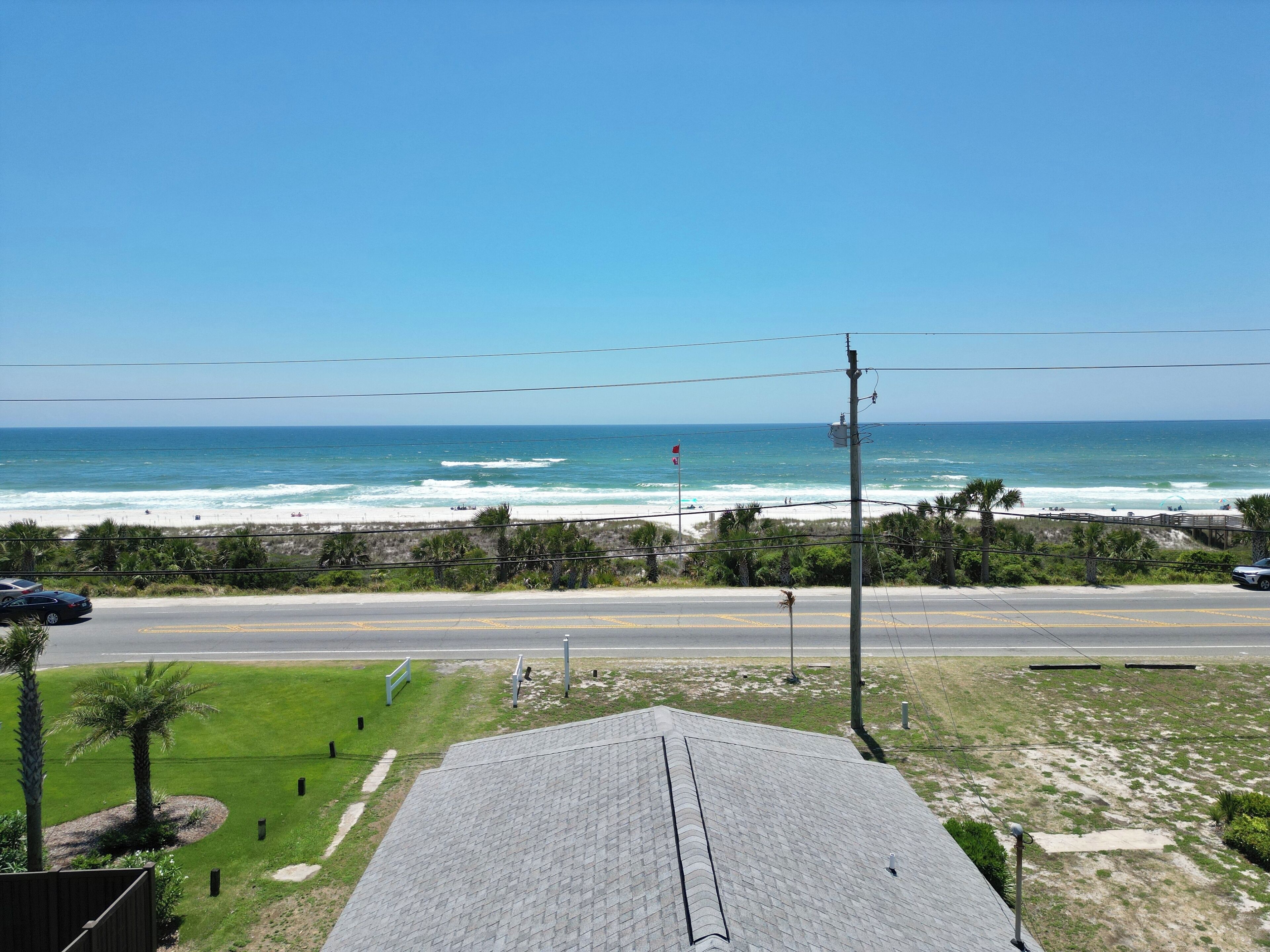 A coastal view with a road leading to the beach, a utility pole, and a grassy area with a building in the foreground.