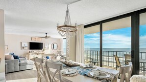 Ein Essbereich mit Meerblick, ein Wohnzimmer mit Sofa und Fernseher sowie ein Balkon mit Geländer.