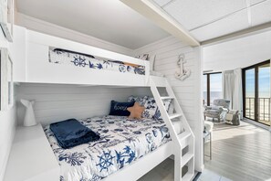 A bunk bed room with nautical-themed bedding, a white wall anchor decoration, and a view of the beach through large windows. - Beautiful Fully Renovated Condo (Panama City Beach)